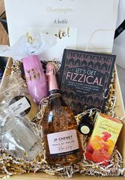 Birthday bubbly gift box with rosé sparkling wine, 'Let's Get Fizzical' cocktail recipe book, pink 'Happy Birthday' flute, gummy bears and glassware nestled in gold-and-white crinkle paper.