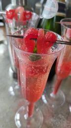 Sparkling pink watermelon cocktail in a champagne flute, topped with a skewered watermelon ribbon and fresh mint — refreshing summer brunch drink.