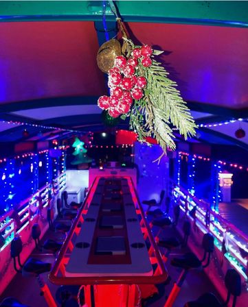 Frosted holly berries and pine sprig hanging over the interior of a holiday-lit pedal party bike, colorful LED lights and a long communal bar table lined with bike seats.