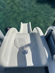 White boat slide with water spilling toward clear green water below, viewed from a pontoon deck on a sunny day — ready to splash into the lake