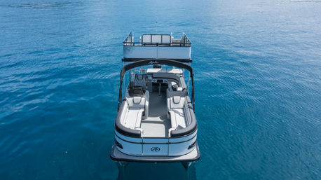 Aerial view of a sleek two-level pontoon boat with white cushioned lounge seating floating on calm deep-blue water