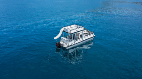 Aerial view of a white pontoon boat with rooftop deck and water slide drifting on calm deep-blue sea