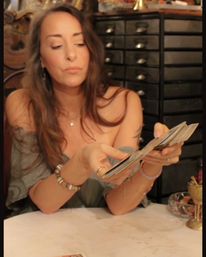 Bohemian tarot reader shuffling tarot cards at a round reading table in a cozy indoor studio with vintage drawers in the background