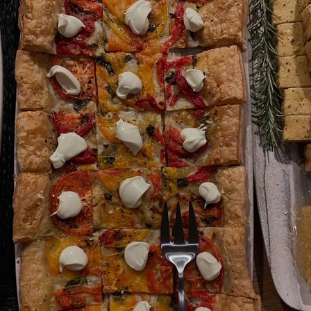 Square-cut puff pastry tart topped with roasted heirloom tomatoes, herbs and dollops of creamy ricotta—gourmet appetizer with serving fork and rosemary garnish