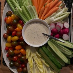 Colorful vegetable platter with cherry tomatoes, celery stalks, baby carrots, sliced radishes, cucumber spears and Belgian endive arranged around a bowl of creamy herb dip — fresh party appetizer.