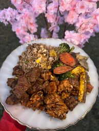 White scalloped plate of mixed stir-fry—grilled beef, chicken, fried rice and vegetables—held outdoors with pink cherry blossom branches in soft focus background