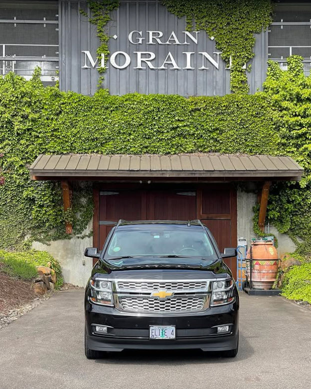 Shiny black Chevrolet SUV parked on a driveway in front of an ivy-covered building with wooden garage doors and a decorative wine barrel