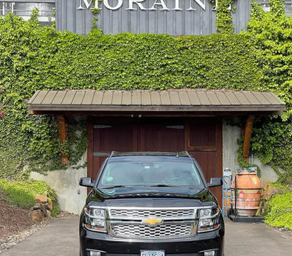 Shiny black Chevrolet SUV parked on a driveway in front of an ivy-covered building with wooden garage doors and a decorative wine barrel