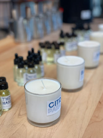 Artisan citrus-scented white candles in glass jars with rows of small fragrance oil dropper bottles on a wooden tabletop