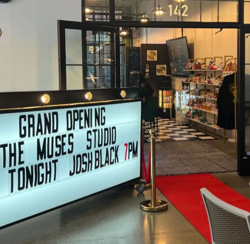 Marquee announcing a grand opening and evening event beside a red carpet leading into an industrial‑chic studio storefront with checkered floor, display shelves, and warm interior lighting.
