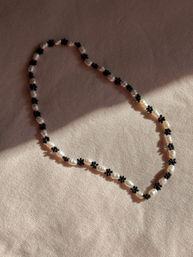 Delicate sunlit pearl necklace threaded with tiny black flower beads, laid on beige fabric