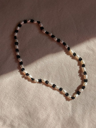 Delicate sunlit pearl necklace threaded with tiny black flower beads, laid on beige fabric