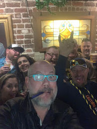 Group selfie of friends at an indoor bar with exposed brick, stained-glass window and beers.
