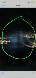 Nighttime phone screenshot with a green hand-drawn circle highlighting a bluish, blurry vertical shape in darkness, flanked by warm streaks of light.