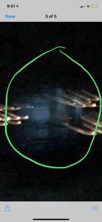 Nighttime phone screenshot with a green hand-drawn circle highlighting a bluish, blurry vertical shape in darkness, flanked by warm streaks of light.