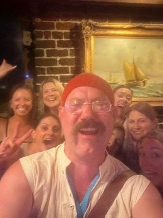 Smiling group selfie in a lively pub with exposed brick and a framed sailboat painting in the background, friends enjoying a night out.