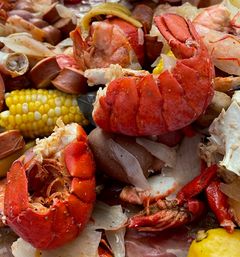Close-up of a seafood boil featuring bright red lobster tails, shrimp, corn on the cob, red potatoes, sliced smoked sausage and onions.