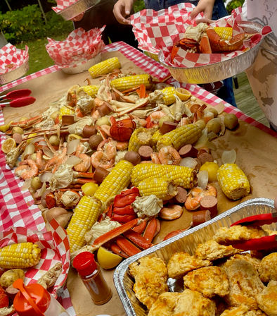 Festive outdoor seafood boil on a picnic table with crab legs, shrimp, corn on the cob, potatoes, sausage, lemon wedges and buttery biscuits