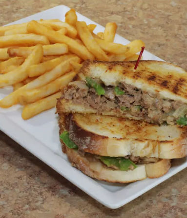 Toasty grilled deli sandwich with shredded filling, melted cheese and lettuce, secured with a toothpick and served with golden French fries on a white rectangular plate.