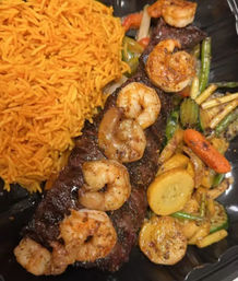 Grilled shrimp-topped steak with seasoned yellow rice and sautéed zucchini, yellow squash, carrots and asparagus on a black plate