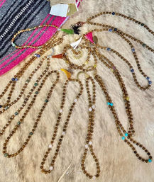 Boho beaded necklaces with warm brown beads, colorful accent stones, tassels and crescent charms arranged on a faux-fur backdrop beside a pink-and-black woven blanket.