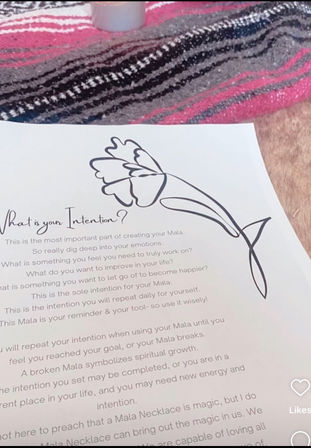 Close-up of a mindfulness worksheet titled What is your Intention? with a simple black floral line drawing on white paper resting on a pink and gray striped blanket, evoking mala intention journaling and self-care.