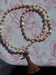 Sunlit boho necklace of light wooden and clear crystal beads with white marbled accents and a tan tassel on pink floral fabric.