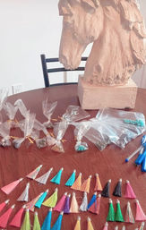 Indoor craft workspace: wooden horse head sculpture on a round wood table surrounded by clear bags of beads, colorful tassel charms, and pens—DIY jewelry supplies on a dining-style table.