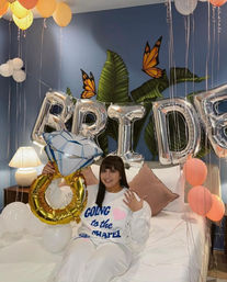 Bride-to-be on a bed in a decorated bridal suite with silver 'BRIDE' balloons, oversized diamond ring balloon, pastel balloons and tropical leaf mural — bachelorette bedroom celebration