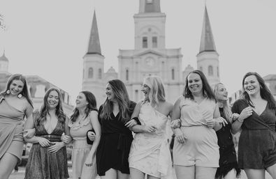 Group of women in summer dresses linking arms and laughing in front of the historic St. Louis Cathedral at Jackson Square, New Orleans — black-and-white photo.
