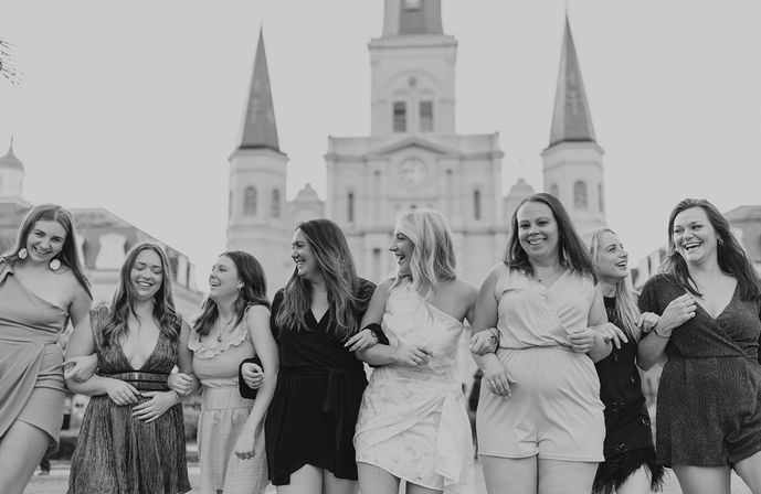 Group of women in summer dresses linking arms and laughing in front of the historic St. Louis Cathedral at Jackson Square, New Orleans — black-and-white photo.