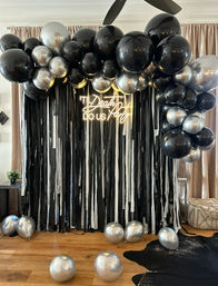 Moody black and silver balloon arch and streamer photo backdrop with neon "Til Death Do Us Party" sign for an indoor party