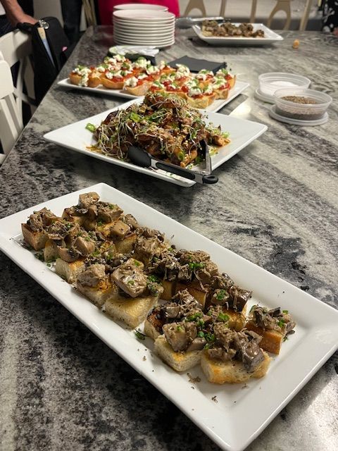 Plated party appetizers on a gray marble kitchen island: crostini topped with sautéed mushrooms and herbs in the foreground, with microgreen-topped crostini and tomato‑mozzarella bruschetta platters behind — ready to serve.