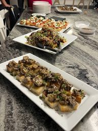 Plated party appetizers on a gray marble kitchen island: crostini topped with sautéed mushrooms and herbs in the foreground, with microgreen-topped crostini and tomato‑mozzarella bruschetta platters behind — ready to serve.