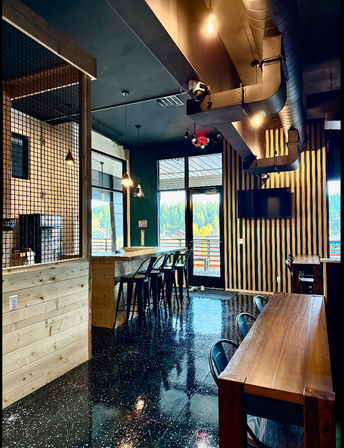Modern cafe interior with wooden bar and high stools, pendant lights, striped wood accent wall, glossy speckled floor, and large windows showing an evergreen forest view.
