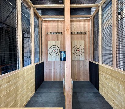 Indoor axe-throwing lanes with wood-paneled walls, safety netting, rubber flooring and two bullseye target boards ready for throwing.
