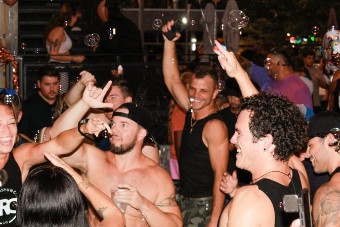 Lively outdoor nightlife scene with a crowd of smiling adults dancing and laughing amid floating soap bubbles at a nighttime party