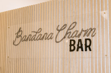 Interior wood-slat wall with acrylic sign showing rope-style cursive script and bold black 'BAR' lettering, warm beige tones