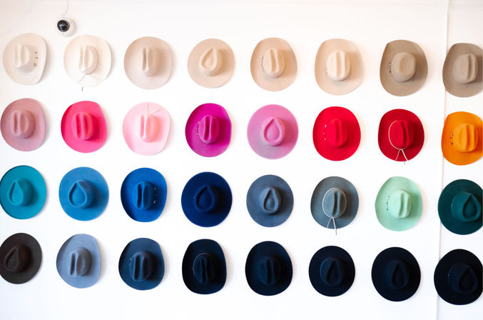 Playful rainbow grid of colorful wide-brim felt hats arranged in neat rows on a white wall