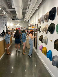 Group of shoppers trying on western-style cowboy hats in a modern hat boutique with a colorful wall display of felt hats, mirrors, wooden counters and polished concrete floors