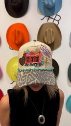 Beige baseball cap with leopard-print brim, turquoise beads and embroidered Las Vegas '777' slot machine patch, worn in front of a colorful cowboy-hat wall display