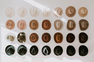Sunlit wall display of neutral-tone cowboy and fedora-style hats mounted in neat rows, ranging from cream and tan to brown and black — stylish boho boutique décor.
