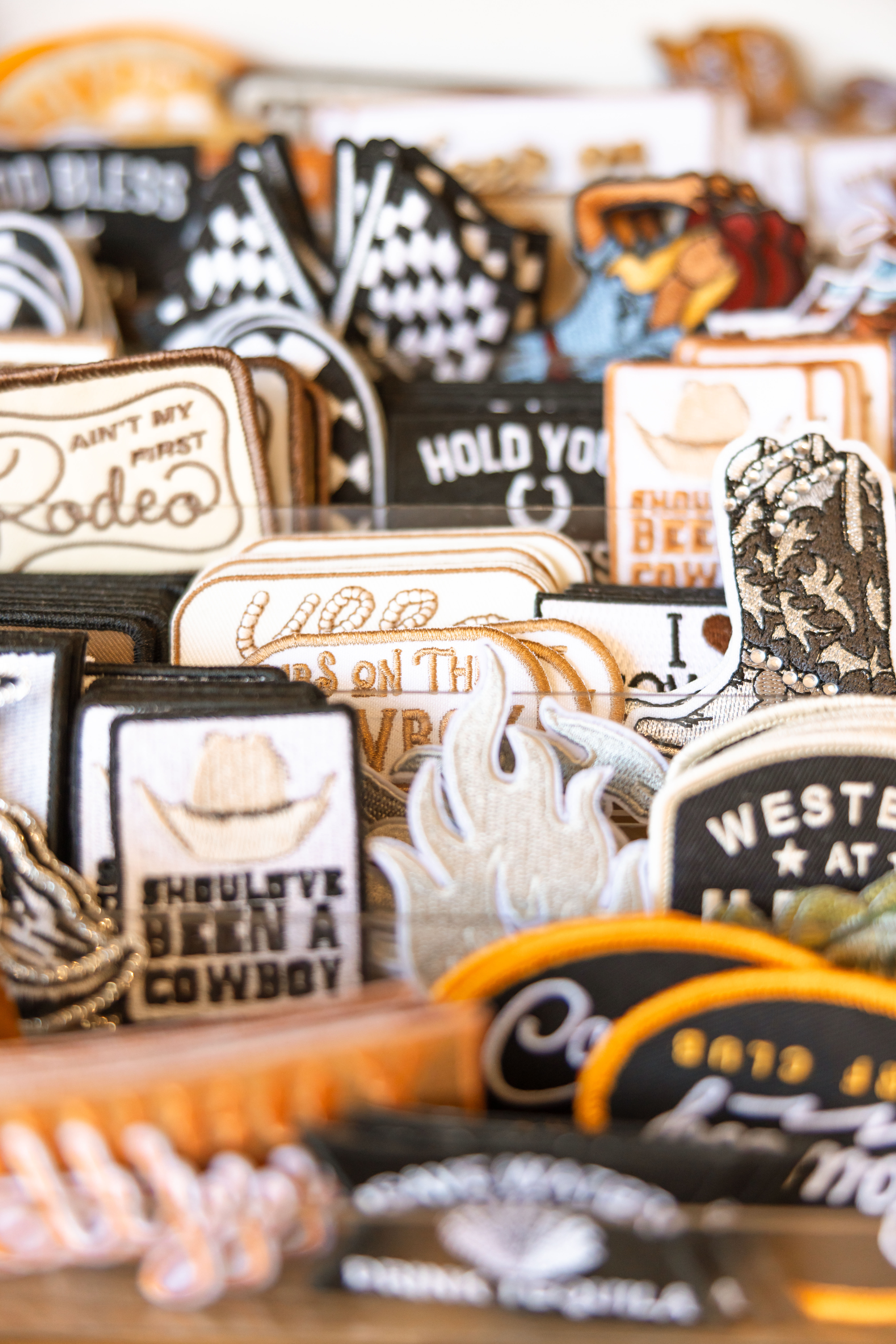 Close-up of embroidered Western souvenir patches — cowboy boots, hats, flames and rodeo slogans — stacked in a colorful market display.