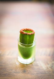 Zesty chili-rimmed cucumber shot — vibrant green fresh cucumber juice served in a small glass with a hollow cucumber garnish, on a wooden table