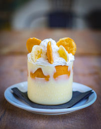 Close-up of creamy banana pudding dessert in a glass jar layered with vanilla wafer cookies, whipped cream and banana slices on a white plate.