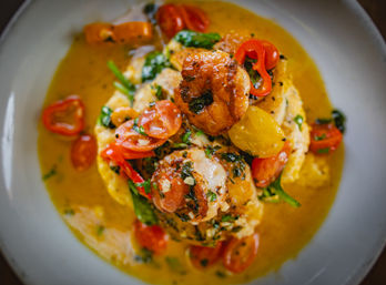Seared shrimp stacked on creamy polenta, topped with roasted cherry tomatoes, fresh herbs and a golden lemon-butter sauce