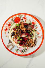 Overhead shot of a colorful beet salad with toasted crunchy grains, microgreens and creamy dressing on a vintage floral plate with a red rim.