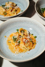 Restaurant-style ricotta ravioli in a creamy tomato-orange sauce topped with grated Parmesan and chopped chives, served in a textured light-blue ceramic bowl