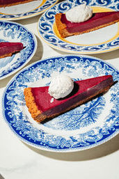 Close-up dessert: slice of red berry tart with graham crust and a dollop of whipped cream on a blue patterned plate