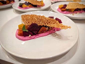 Fine-dining plated appetizer: vibrant pink beet purée with roasted red and golden beet cubes, a crunchy sesame tuile and microgreens on a white plate.